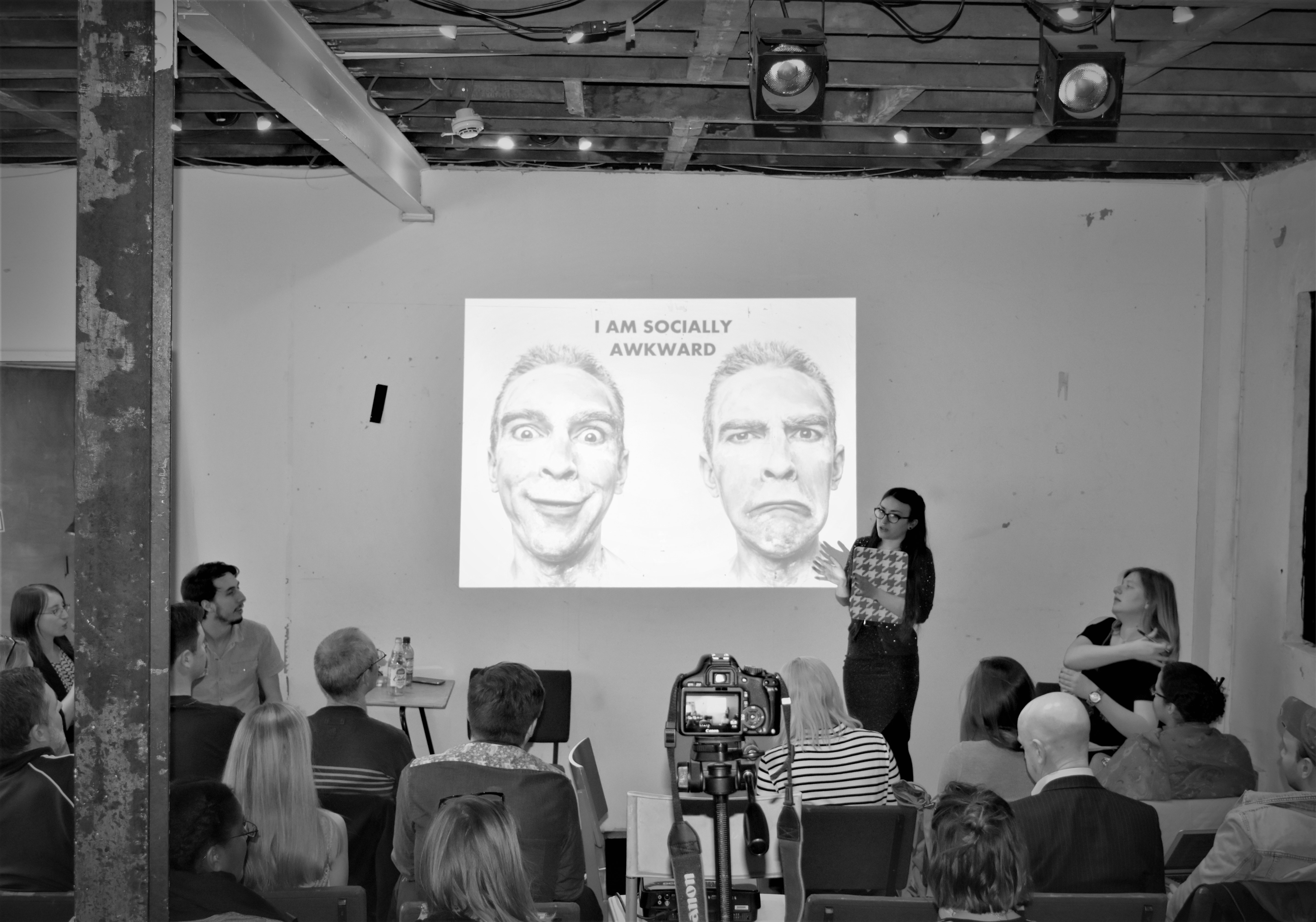 Honor is standing in front of a screen that says 'I am socially awkward' - but it's actually a talk about doing the stuff you're most uncomfortable with