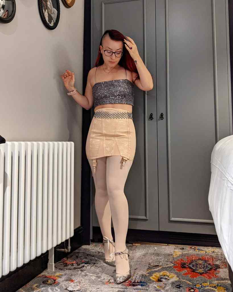 Honor wearing a pink Gossard girdle with ballet tights, a gunmetal sequin crop top and silver Betsey Johnson heels