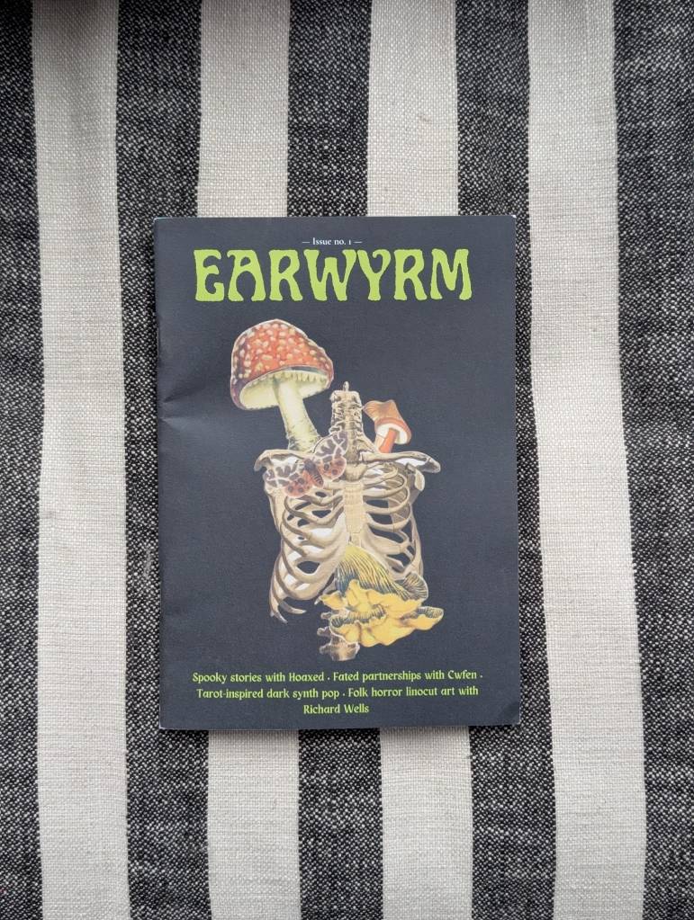 A zine titled 'Earwyrm' featuring an illustration of a skeleton intertwined with a mushroom, resting on a striped background. Tagline includes 'Spooky stories with Hoaxed' and other thematic descriptions.